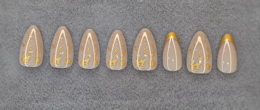Press on nails with nude base, white lines, and gold foil accents on gray background