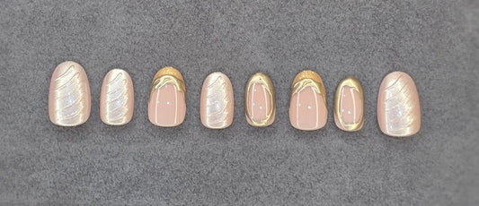 Set of press-on nails with nude, gold metallic, and iridescent swirl designs on gray background