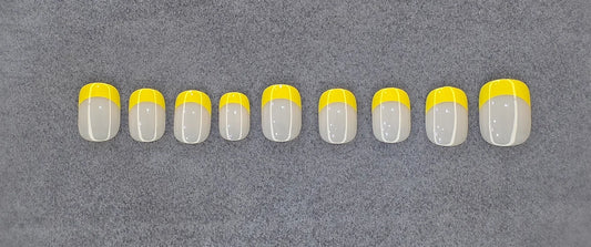 Set of yellow French tip press-on nails arranged on a gray textured background