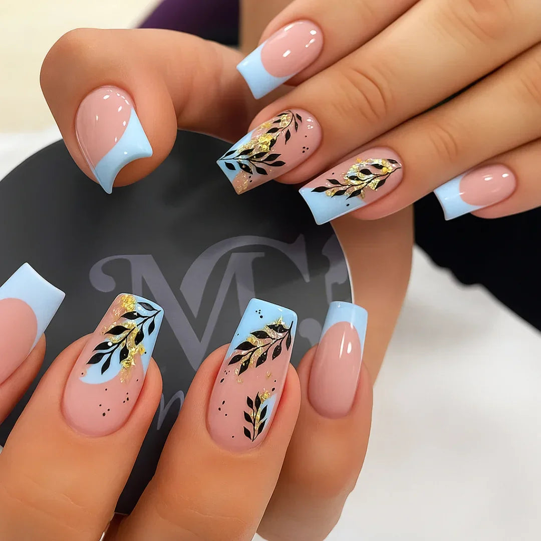 Light blue French tip nails with black and gold floral foil accents, nude base manicure.