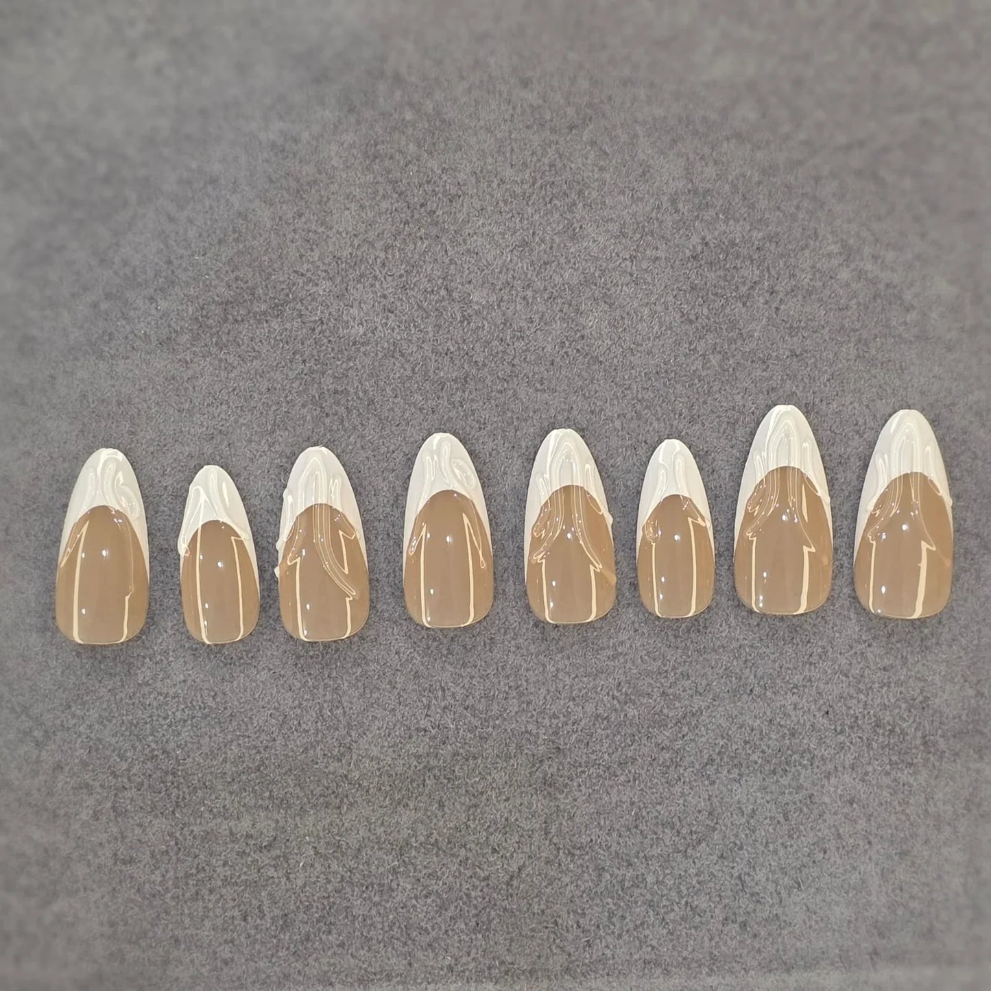 Set of glossy beige and white press-on nails with abstract swirl design on gray background