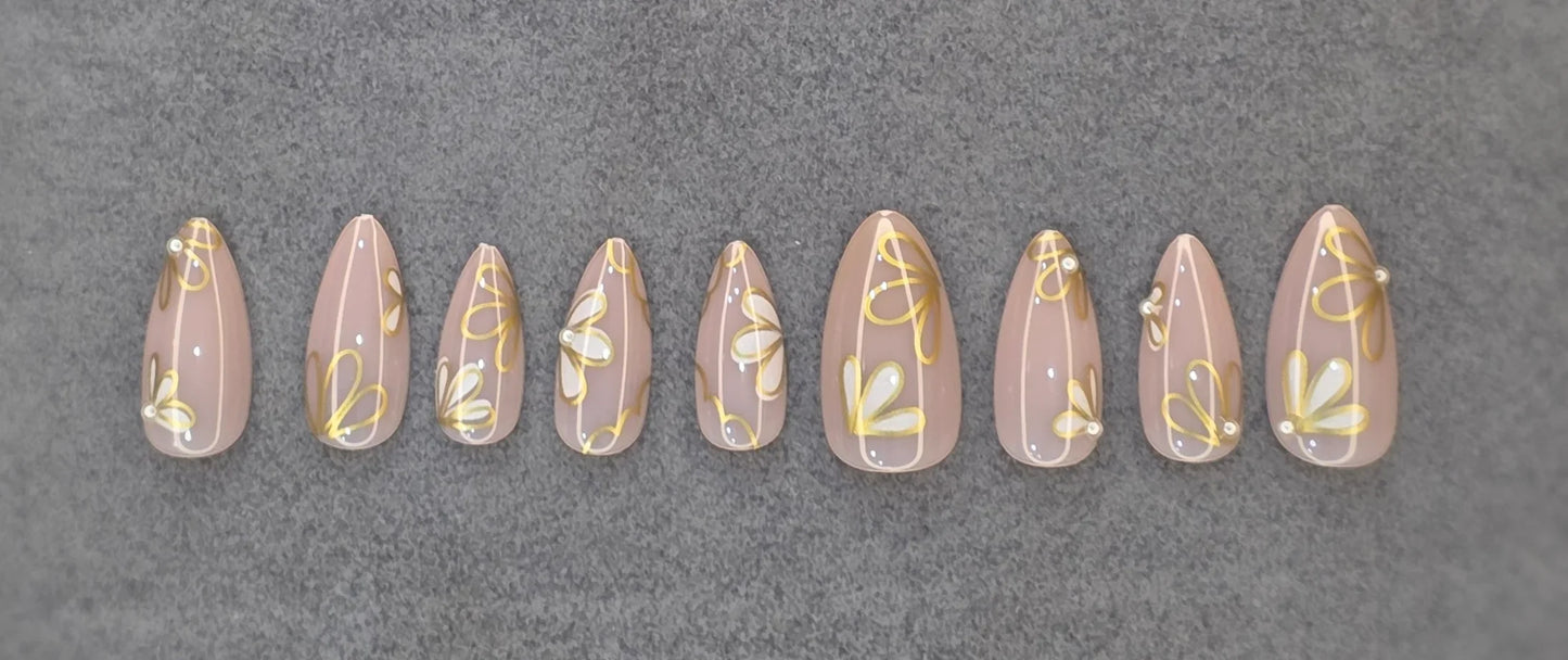 Glossy nude press-on nails with gold and white daisy floral French tip design