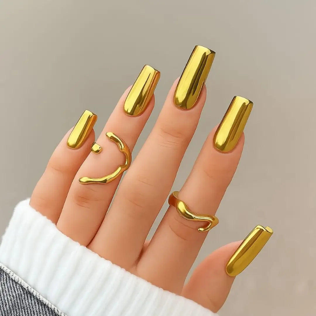 Hand with long gold chrome mirror nails and gold rings, trendy nail design
