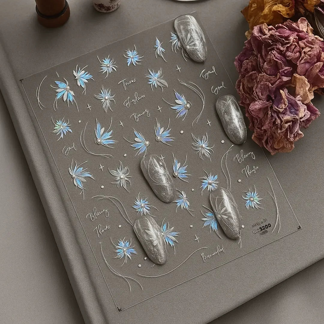 Holographic blue floral nail stickers with silver designs and dried flowers on a gray surface