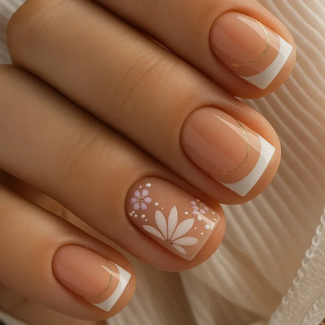 Nude French manicure with white tips, gold accents, and floral nail art on short nails
